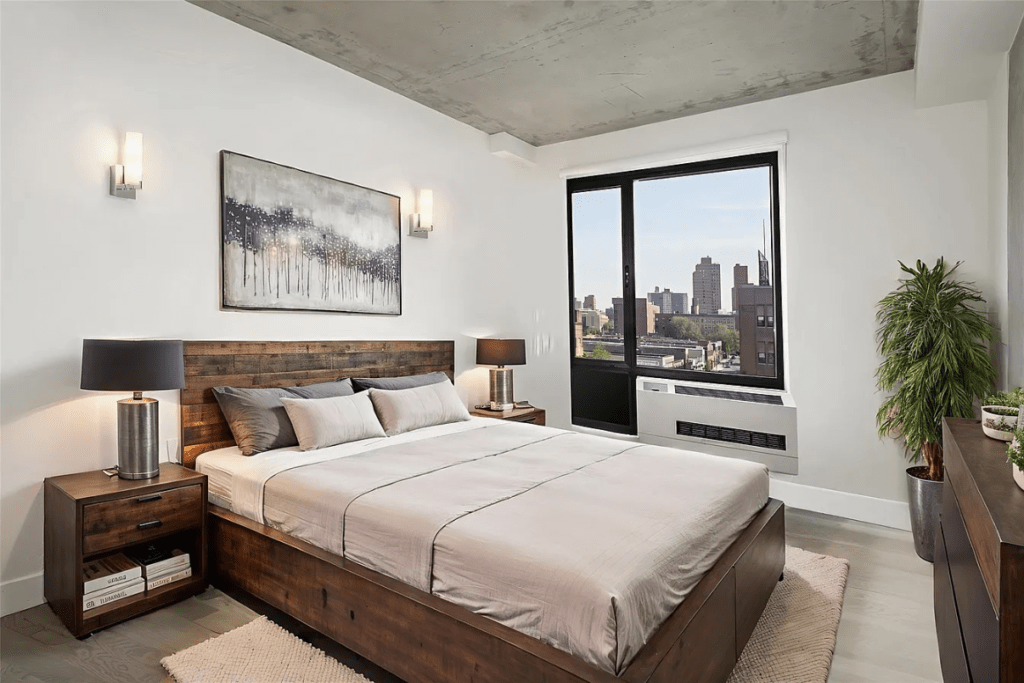 Modern bedroom featuring a wooden bed, nightstands, and a large window with city views