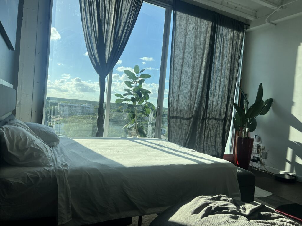 Bright bedroom with a large window showcasing a blue sky and greenery outside